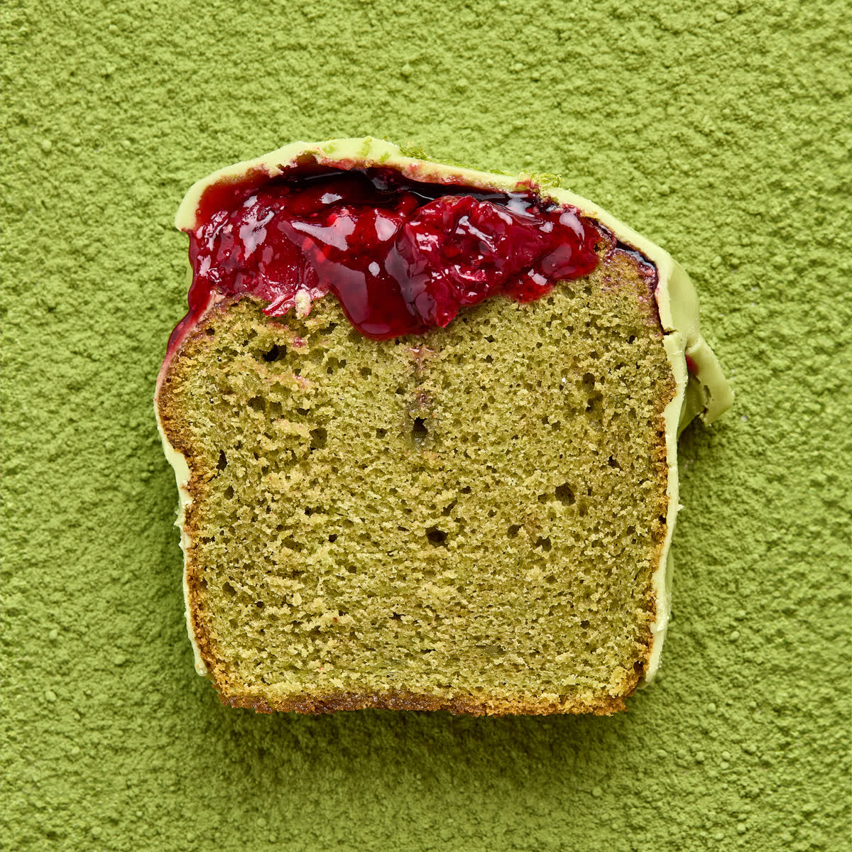 Slice of matcha cake with raspberry on a green background